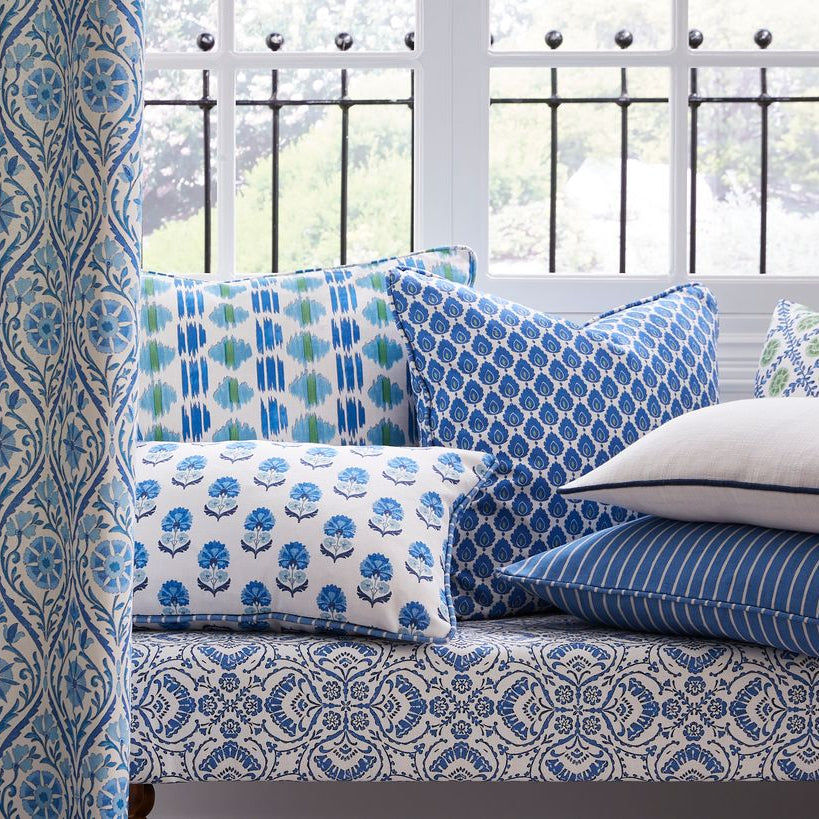 Decorative pillows with blue and white patterns on a bench by a window.