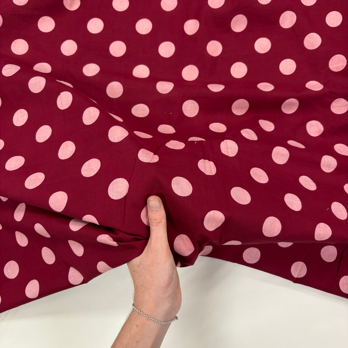 Burgundy Spotty Indian Print Cotton Fabric, with hand for scale. Lightweight 100gsm printed cotton for dressmaking, handmade gifts, crafts and soft furnishings, handcrafted using traditional Indian printing techniques.