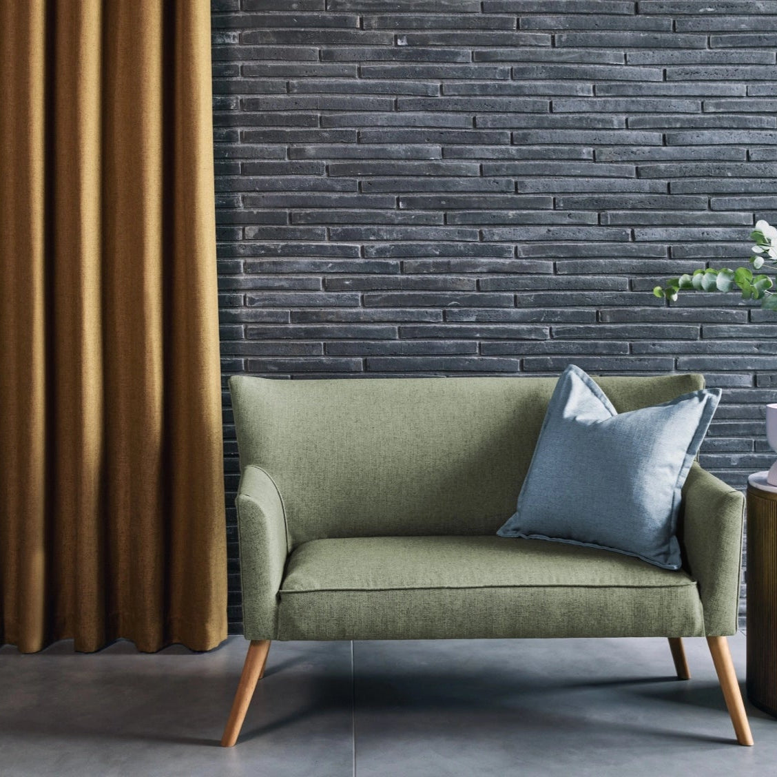 Green sofa with a blue pillow against a textured wall with a curtain.