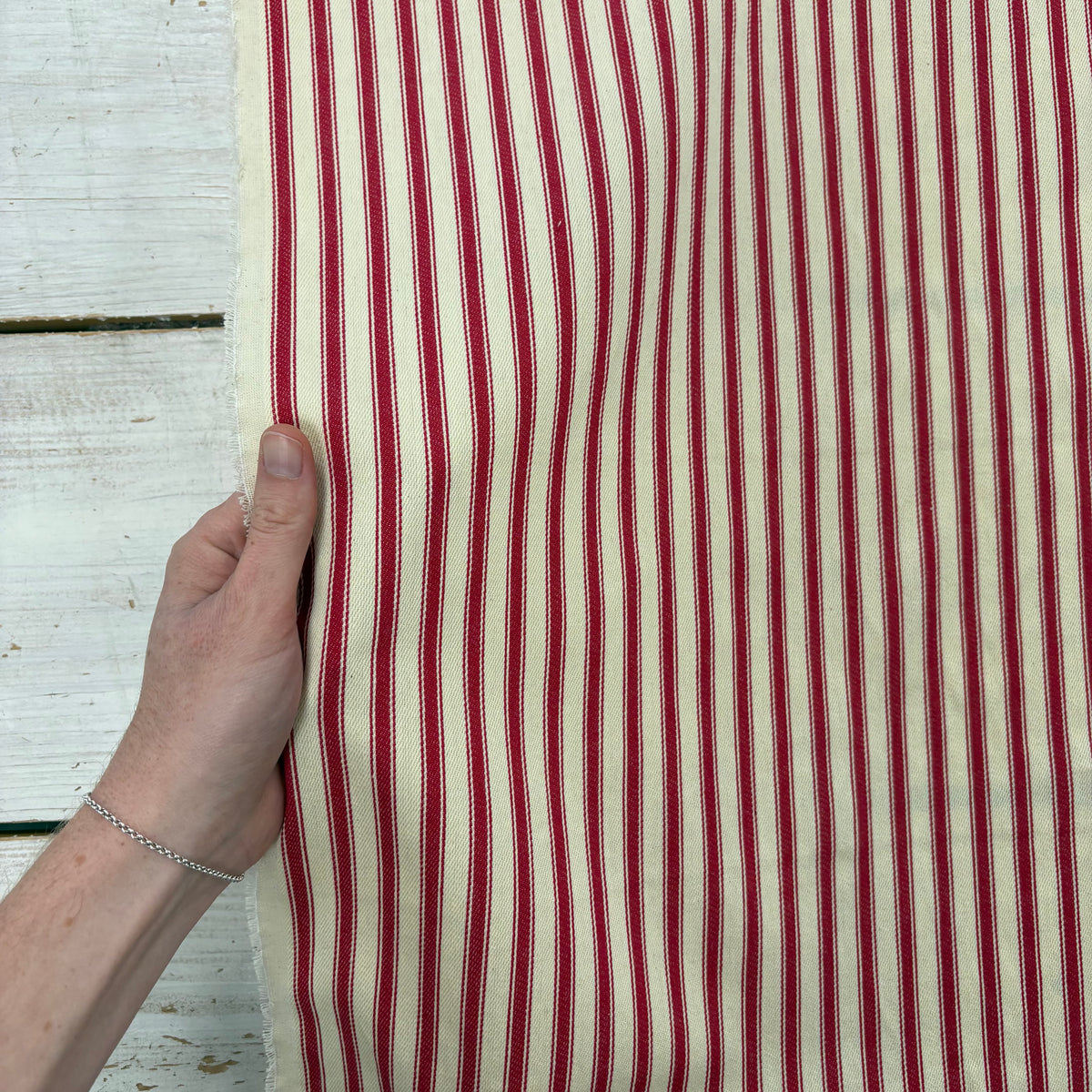 Classic red cotton ticking fabric with traditional stripe design with hand for scale, ideal for cushions, tablecloths, table runners, lampshades, home furnishings and DIY craft projects.