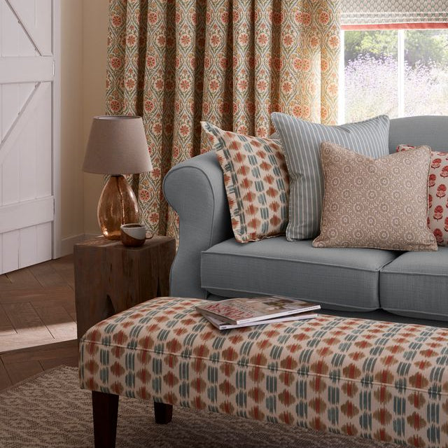 Living room with a gray sofa, patterned cushions, and matching ottoman under a floral curtain.