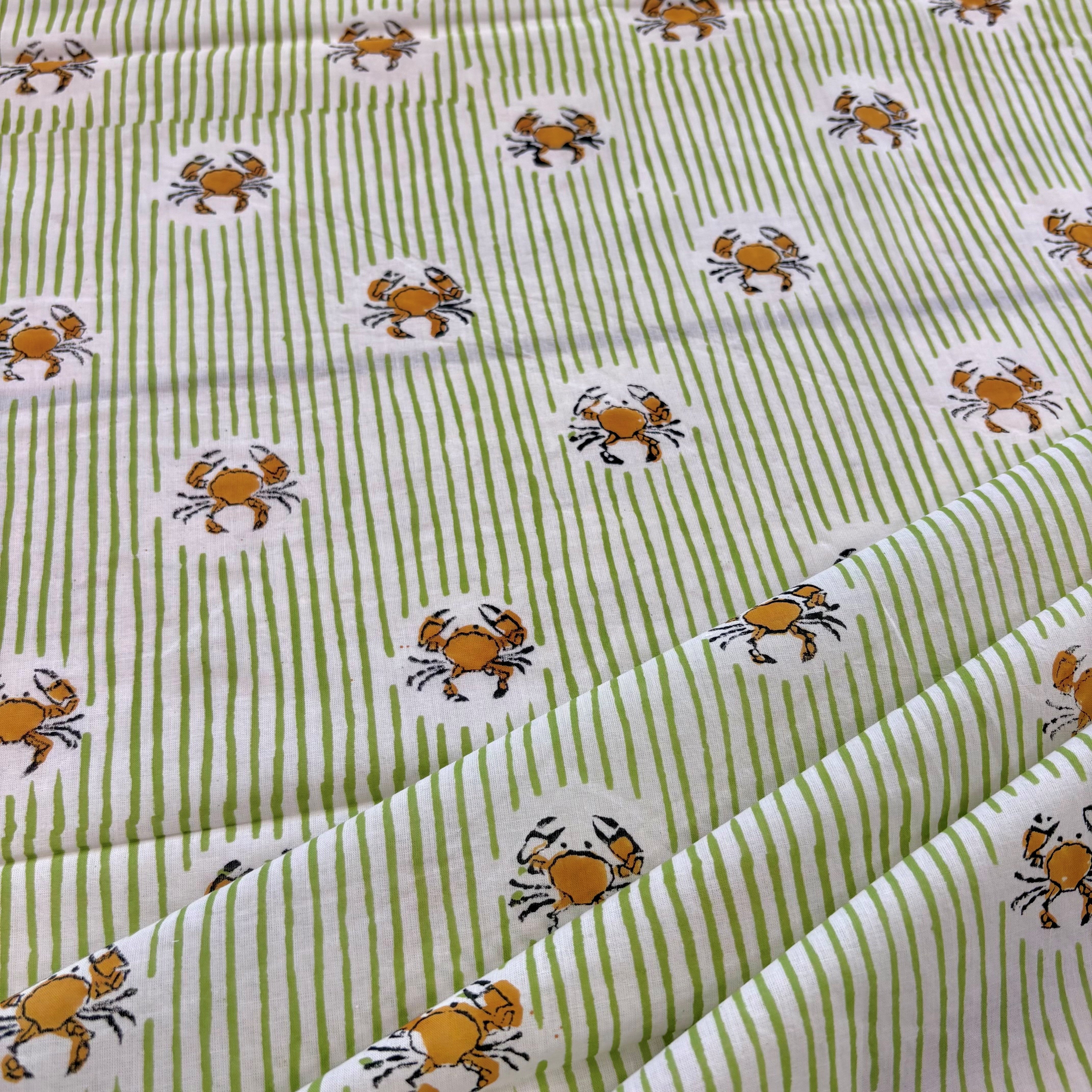 A close-up of a fabric with a pattern of light green and white vertical stripes, decorated with small cartoon crabs in orange, yellow, and black.
