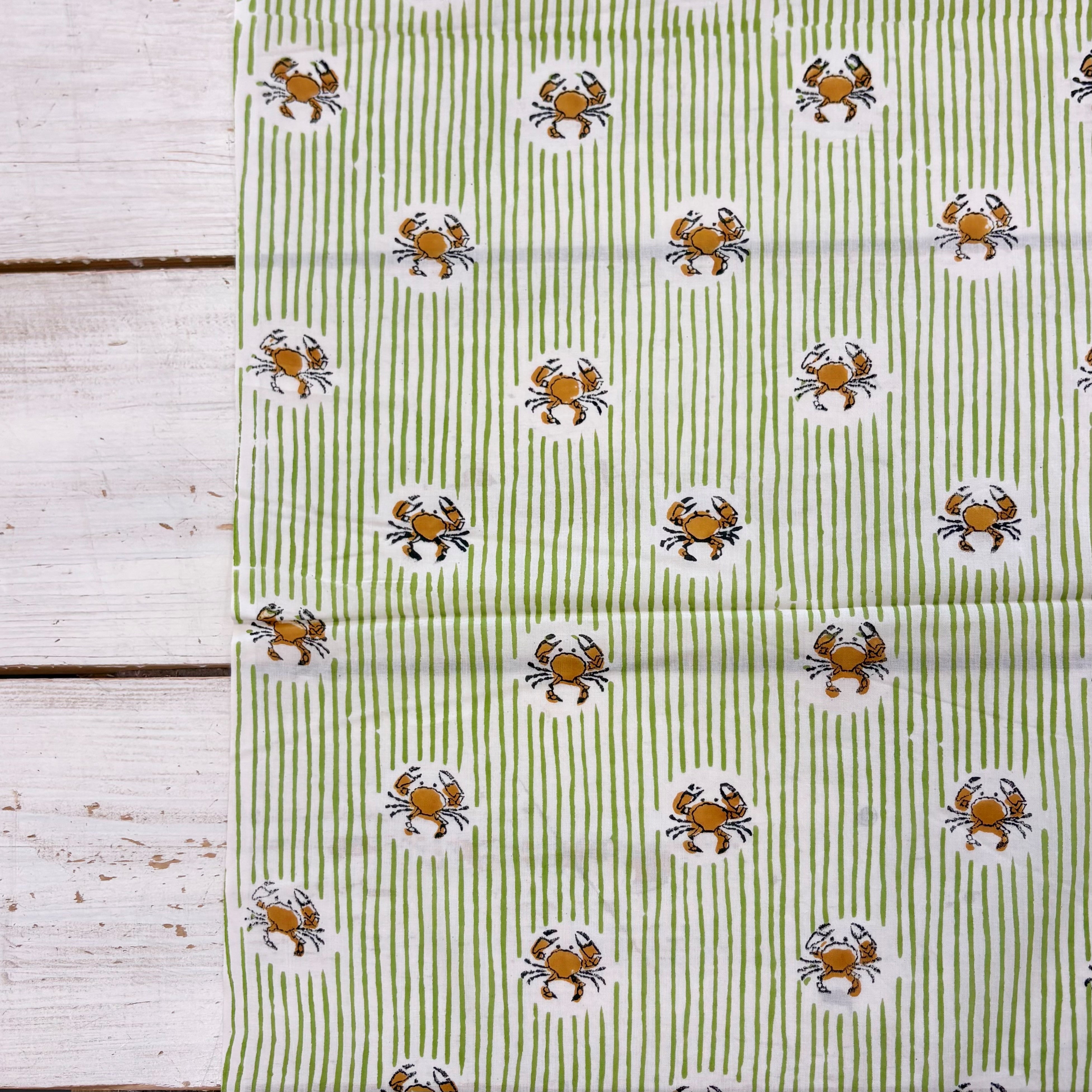 Fabric featuring a green and white striped pattern with orange and black crab illustrations, laid flat on a white wooden surface.