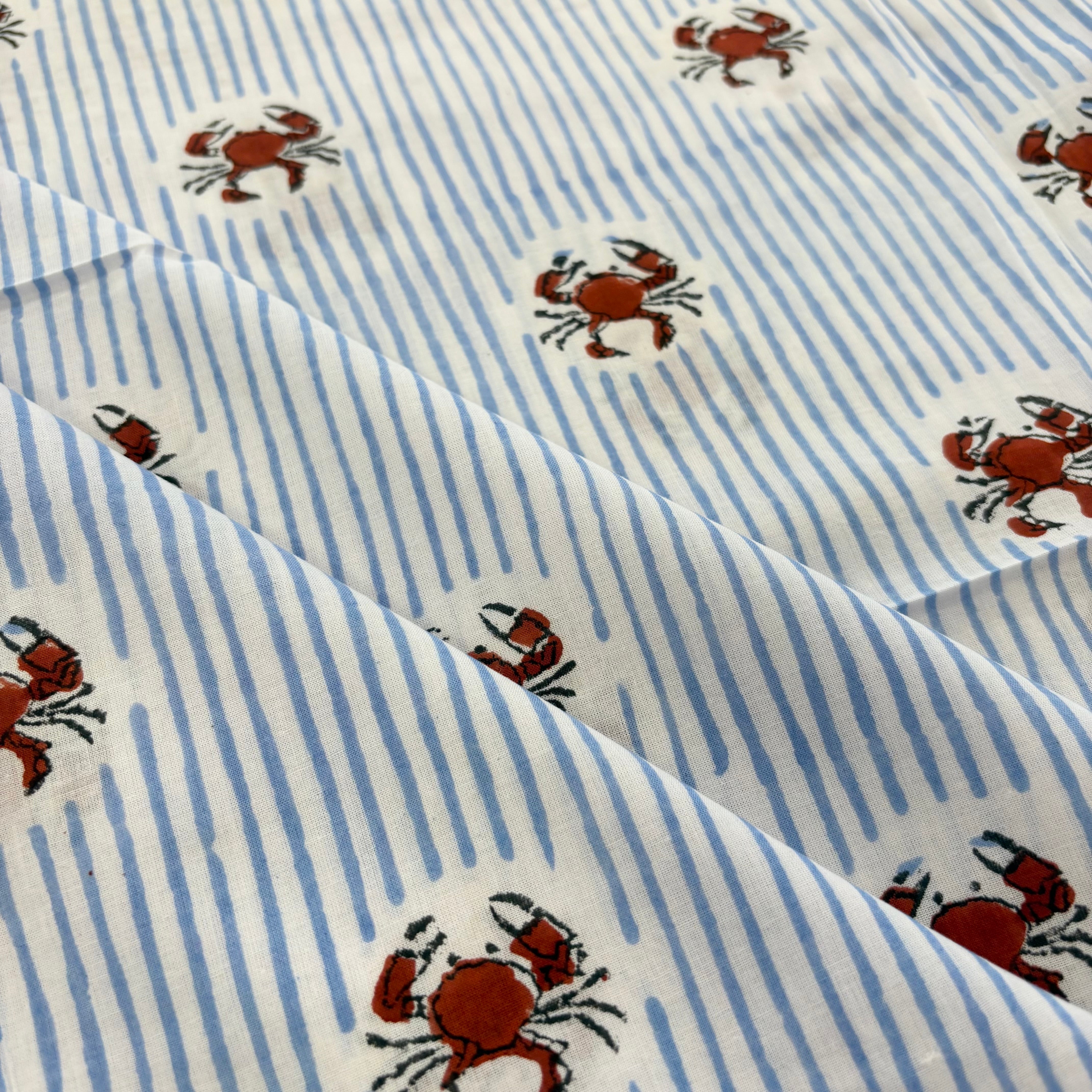 A close-up of a fabric pattern featuring light blue and white vertical stripes with scattered brown crabs on a white background.