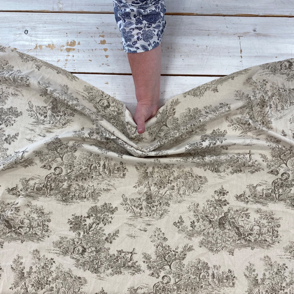 Person holding a large piece of patterned fabric on a wooden table