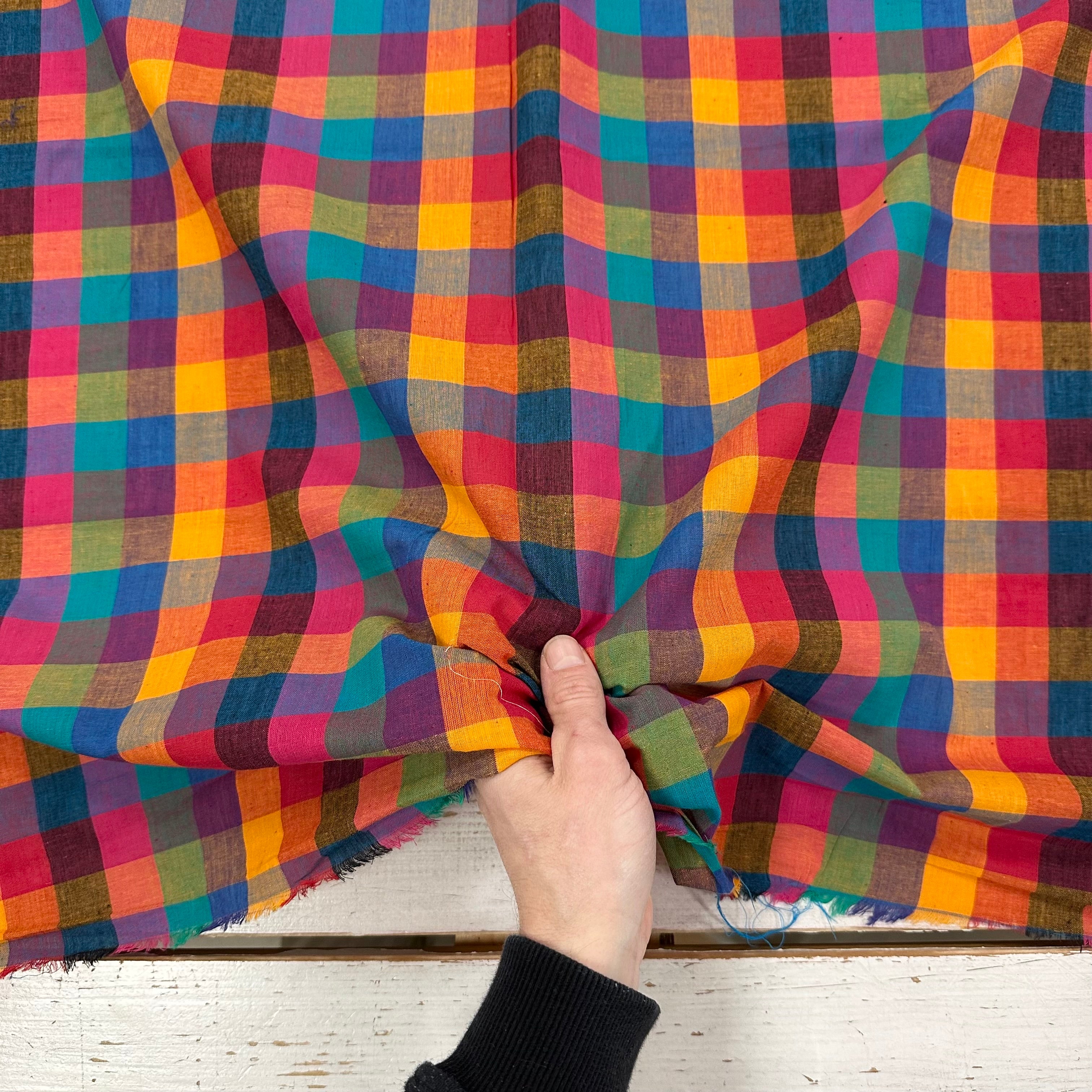 Multicolored checkered fabric with a hand holding it, on a wooden surface.
