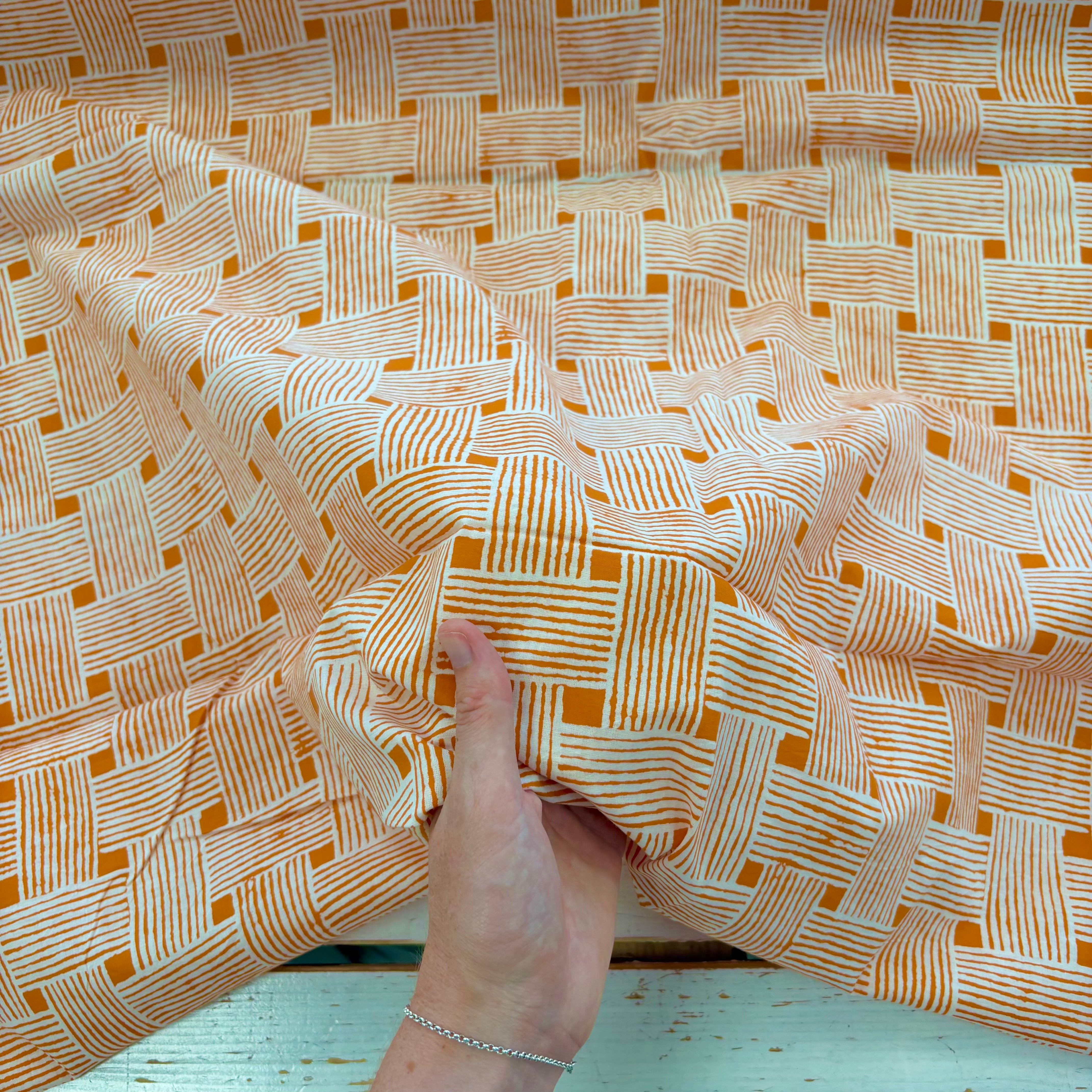 A close-up of a hand holding up a piece of fabric with a woven basketweave pattern in orange
