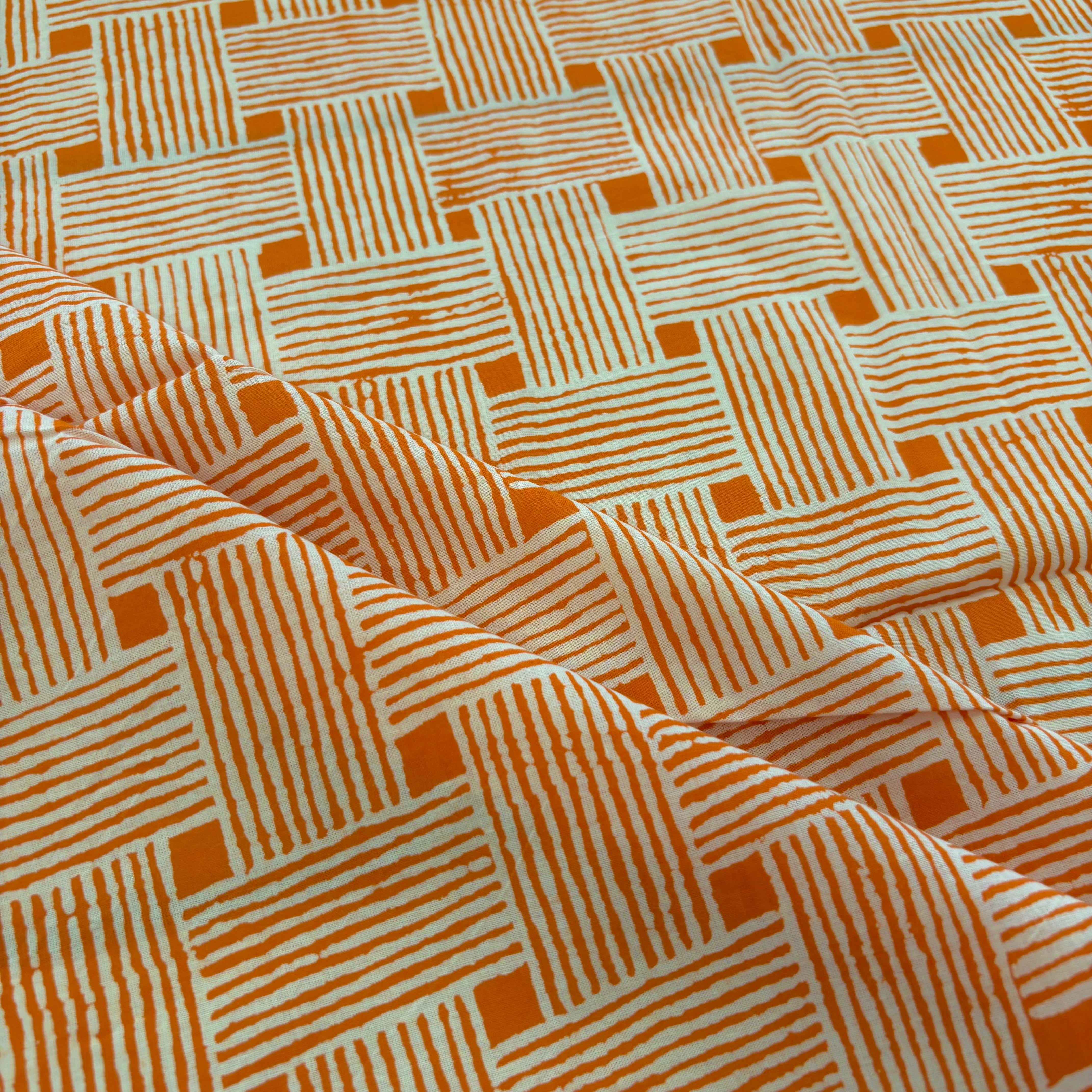 A close-up of patterned fabric with an orange and off-white geometric basketweave design, shown with soft folds.