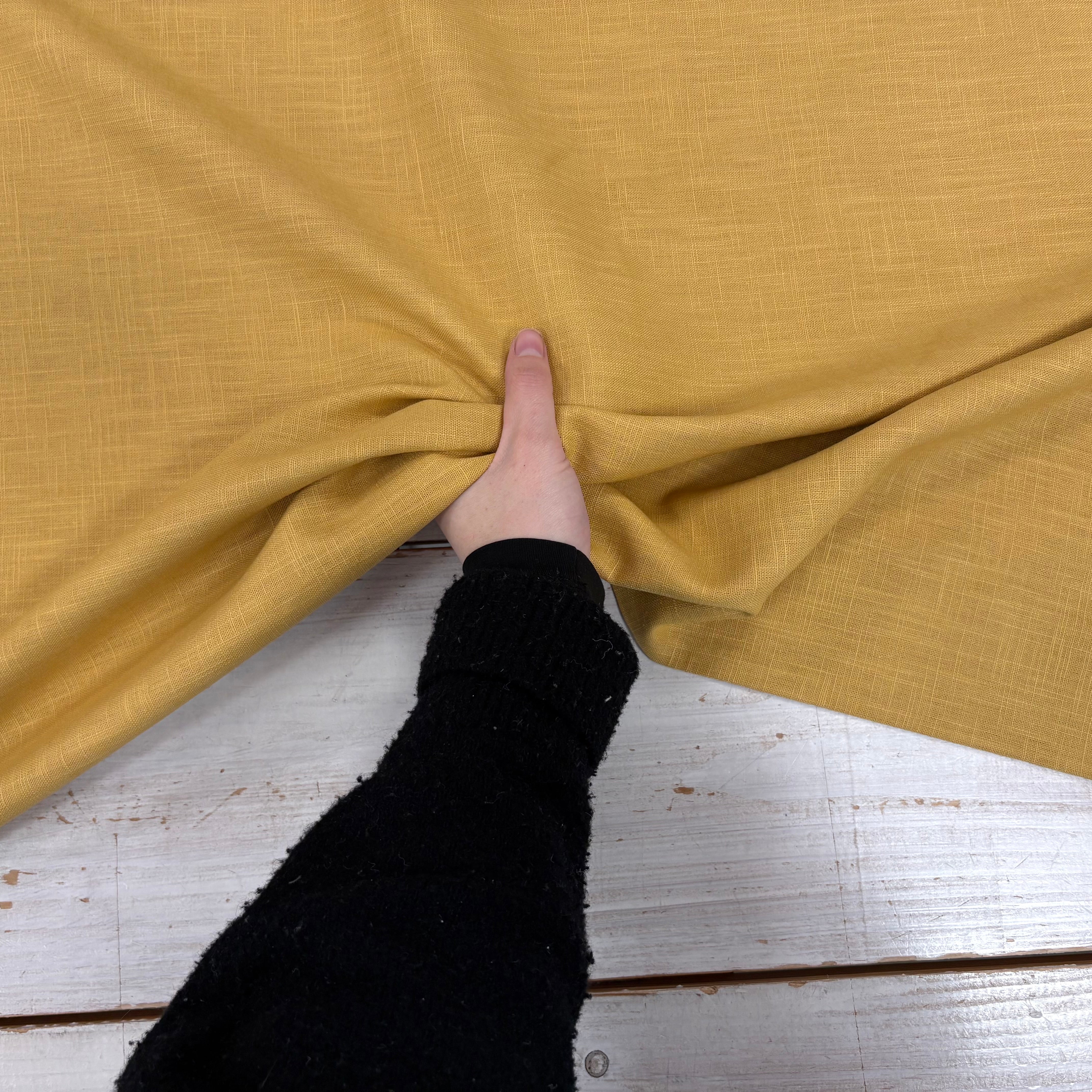 Mustard ramie linen dress fabric with a natural woven texture being held to show movement