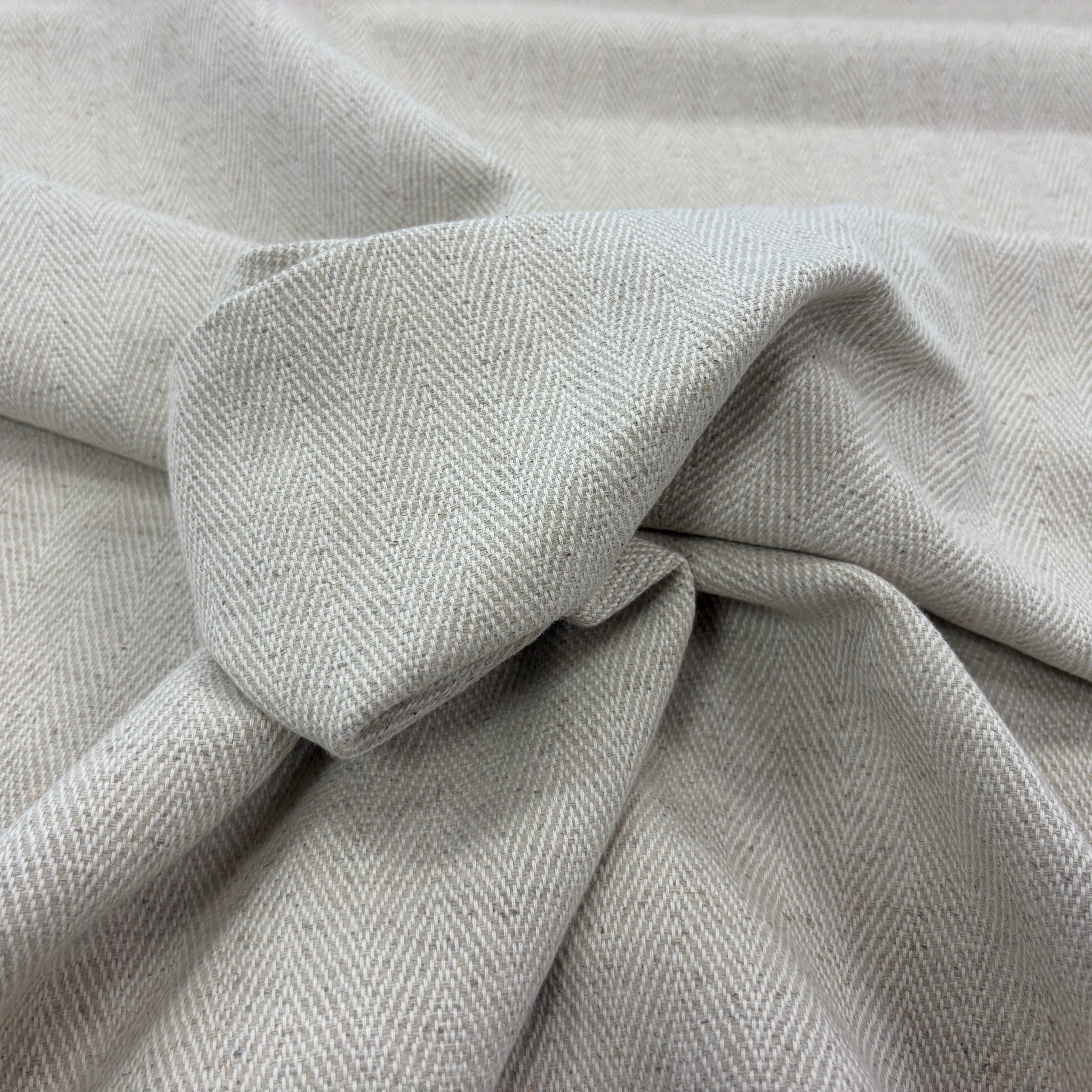 A close-up of draped linen with a subtle herringbone texture, arranged in soft folds.