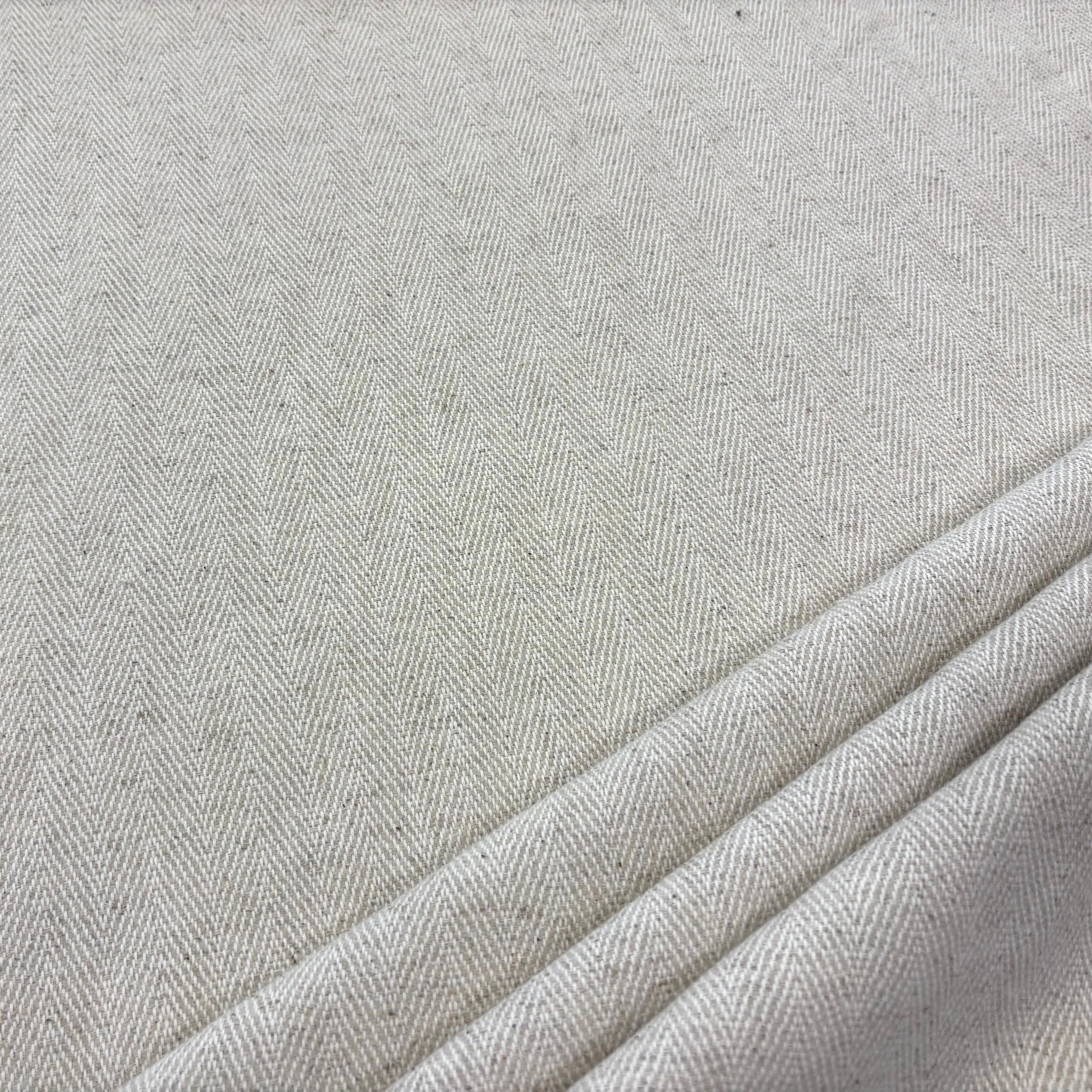 A close-up of light beige fabric with a fine herringbone weave and soft folds along the lower right corner.