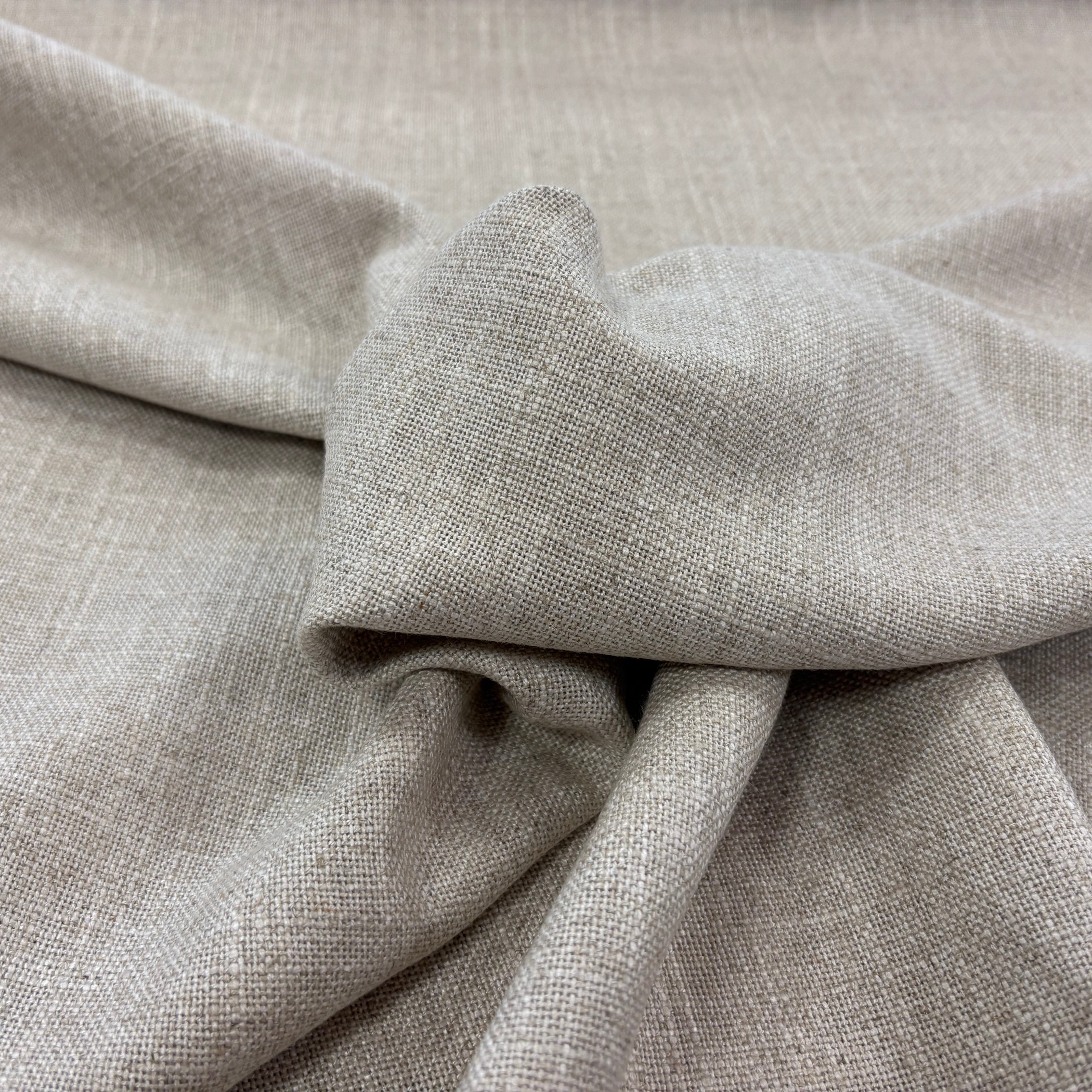 A close-up of draped light beige linen fabric with a visible woven texture and soft folds.