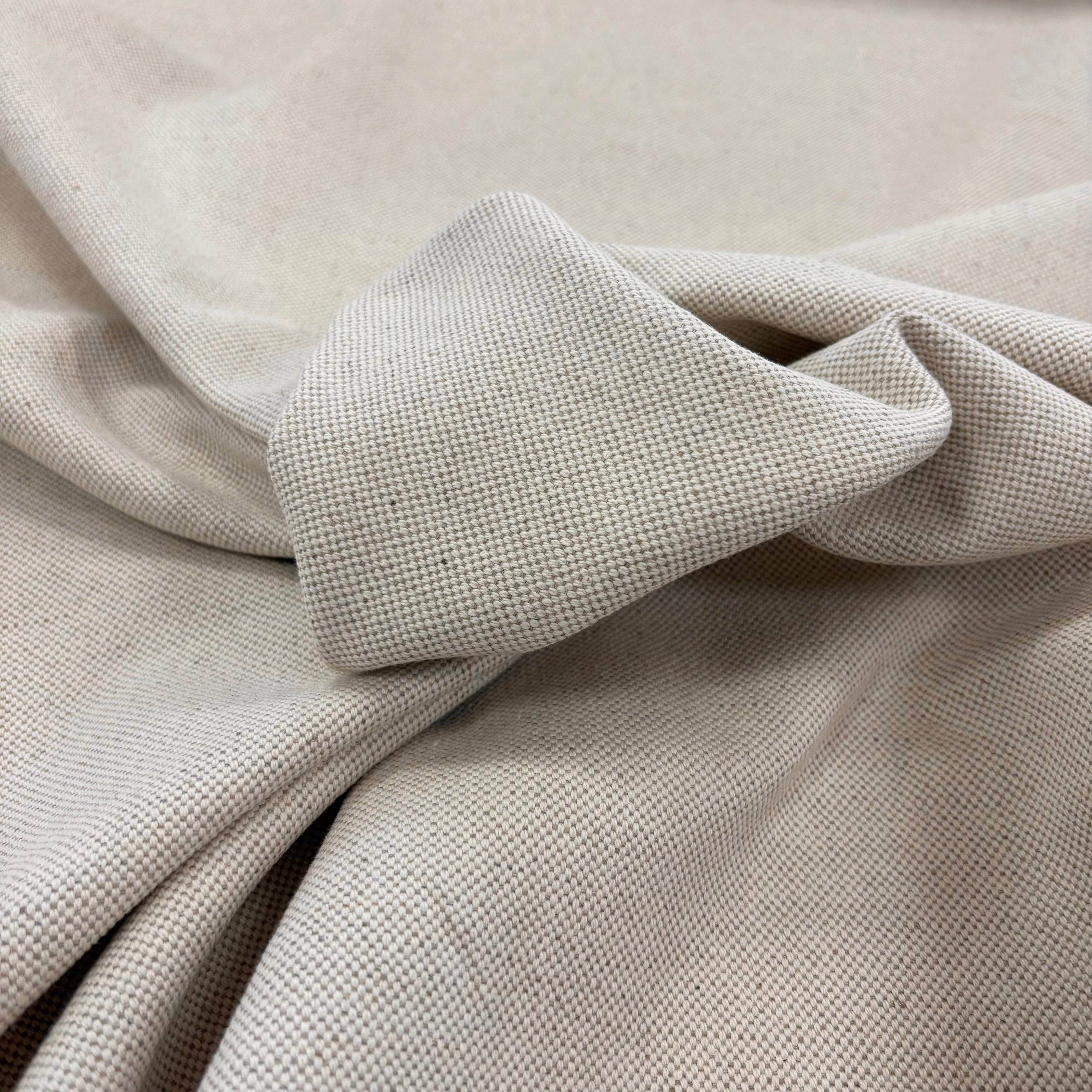 A close-up of linen woven fabric in a light neutral tone, showing the textile texture and soft folds.