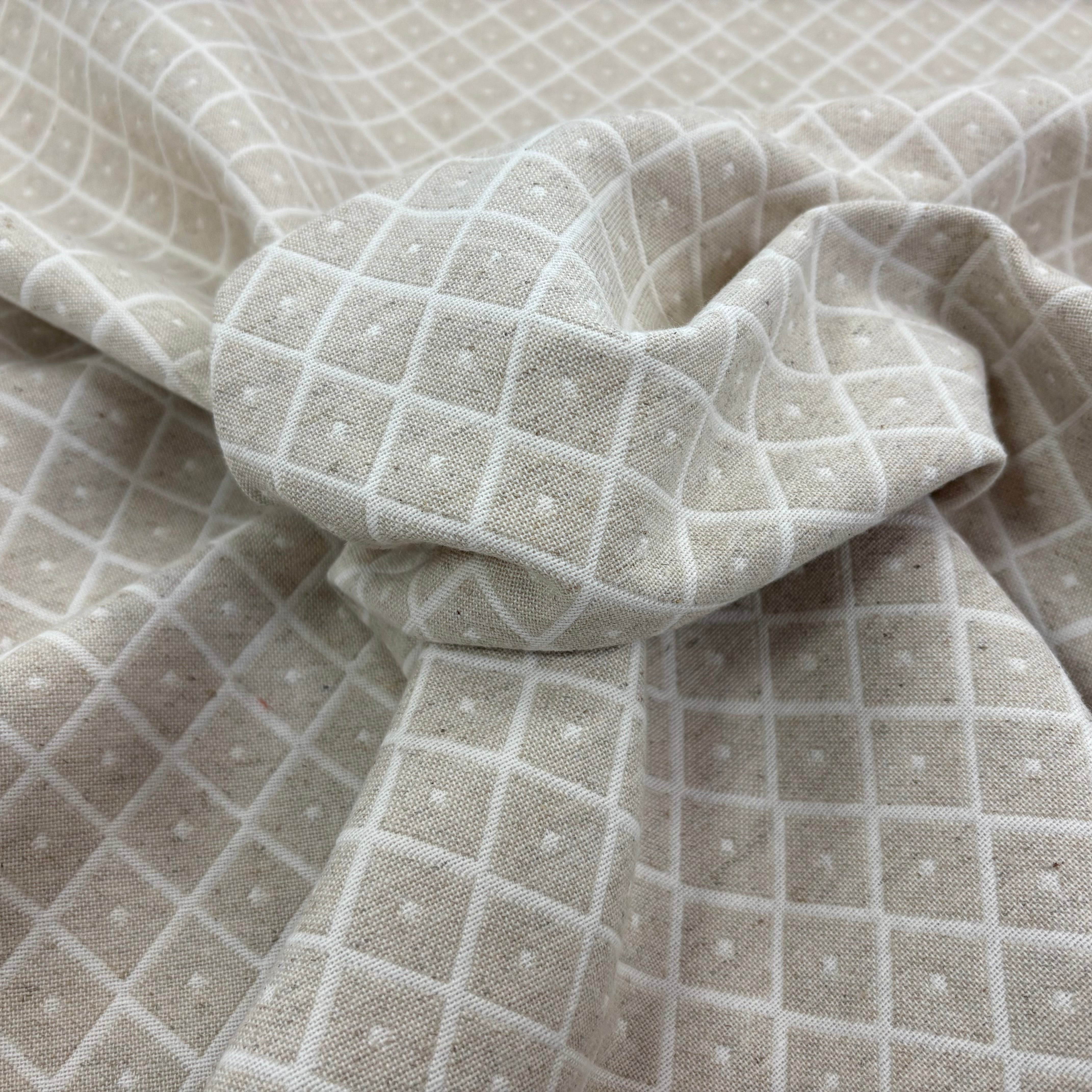 A close-up of draped fabric with a light beige base and diamond weave