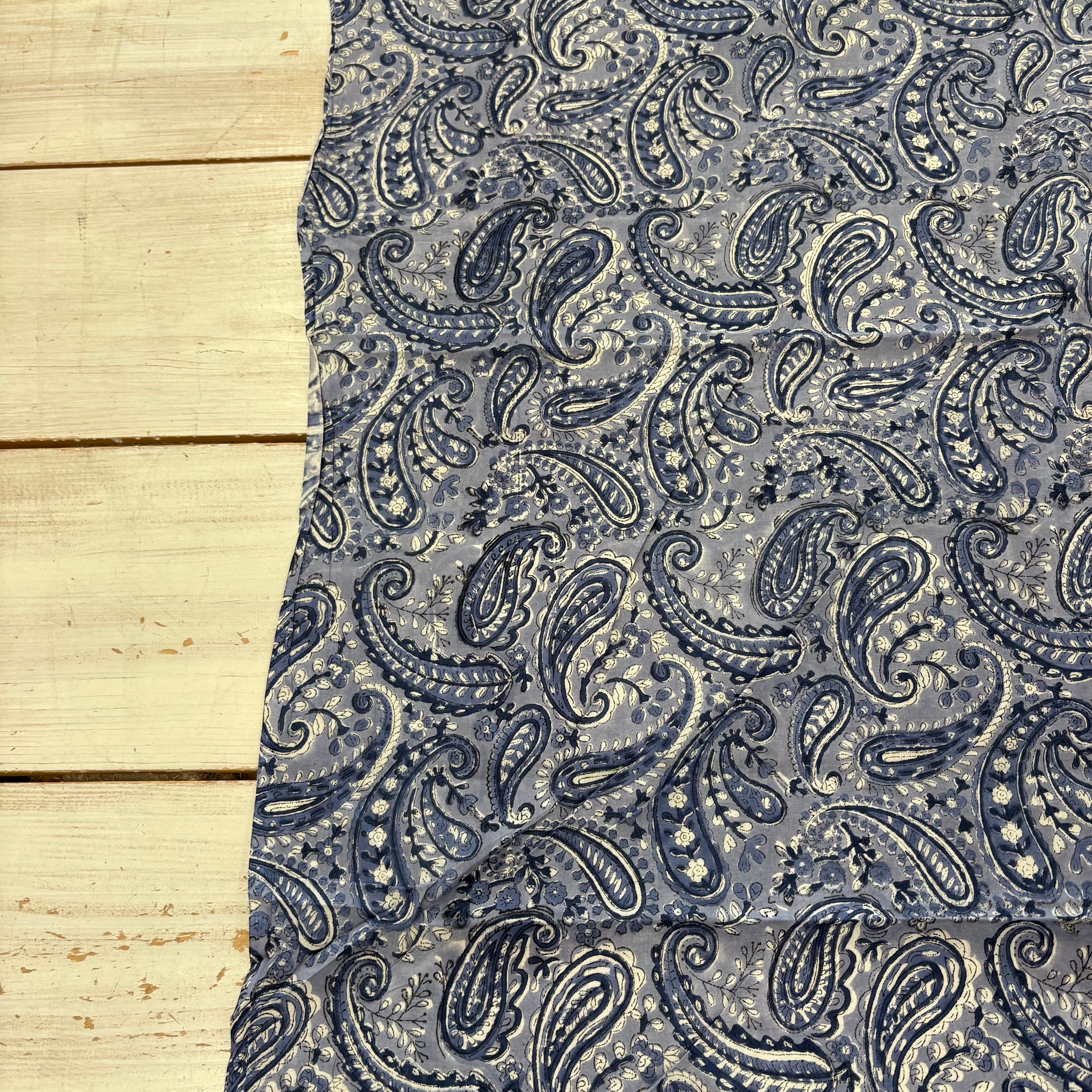 A piece of fabric with a blue paisley pattern, laid flat on a light-colored wooden surface.