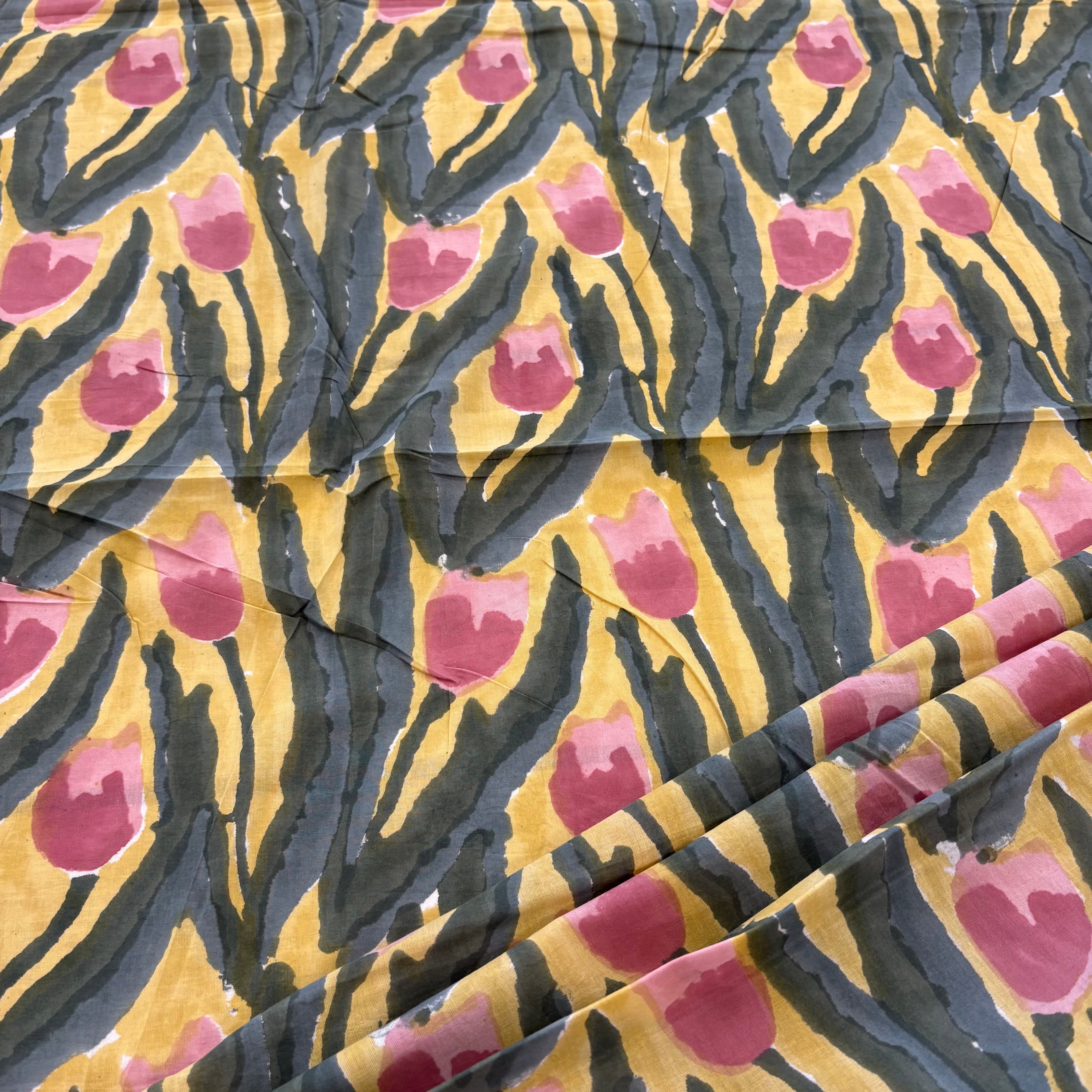 A close-up of patterned fabric with a mustard yellow base, green abstract brushstroke shapes, and pink tulip motifs.