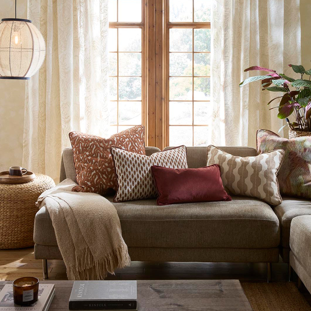 Zafira Living rooms set. A cozy living room scene featuring a beige sectional sofa styled with patterned throw pillows, a rust red accent pillow, and a cream throw blanket.