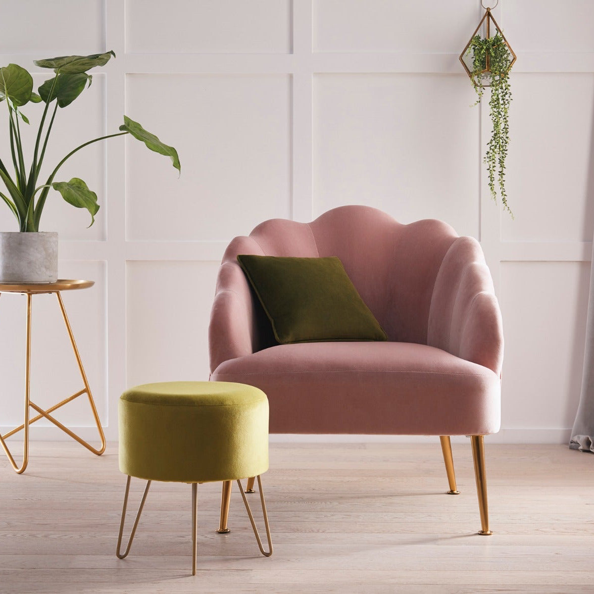Pink armchair with a green cushion in a room with a plant and small table.