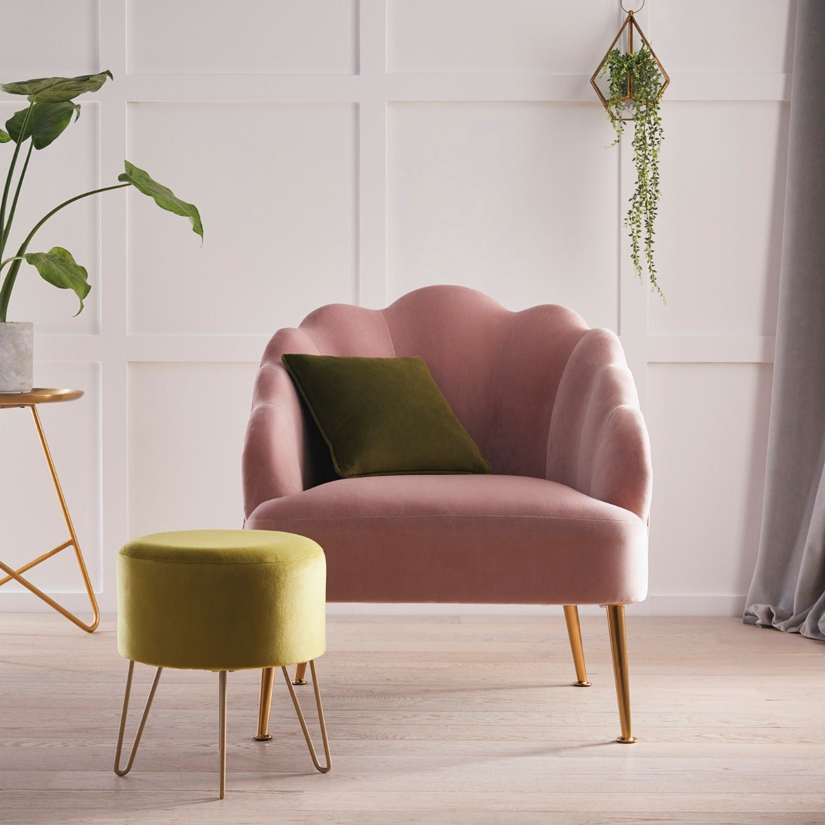 Pink armchair with a green cushion in a room with a plant and small table.