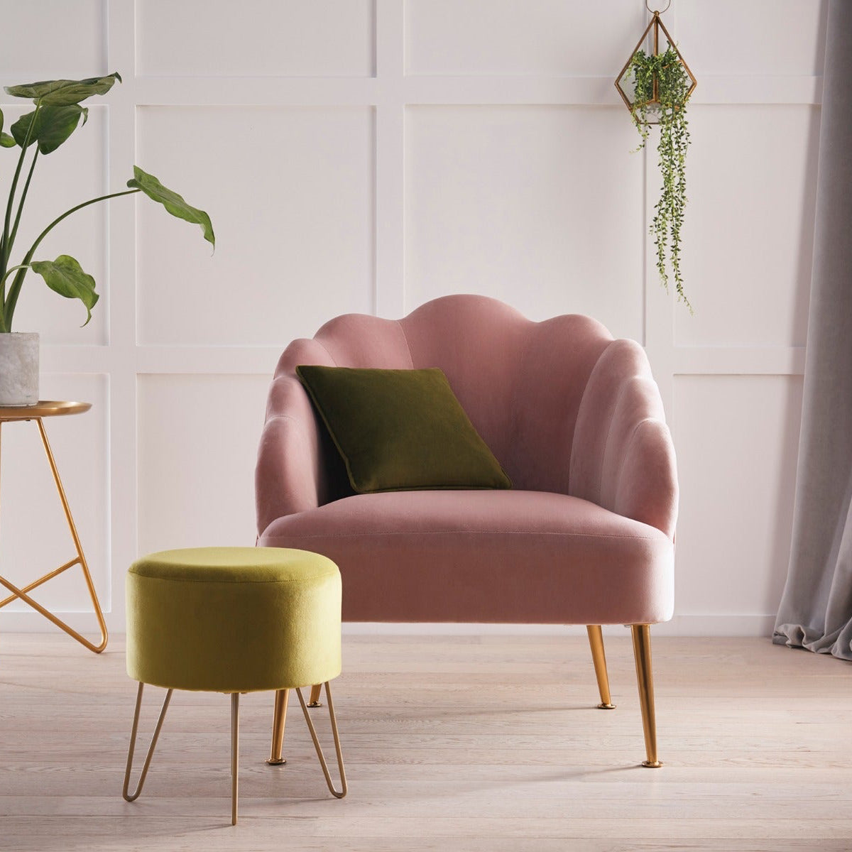 Pink armchair with a green cushion in a room with a plant and small table.