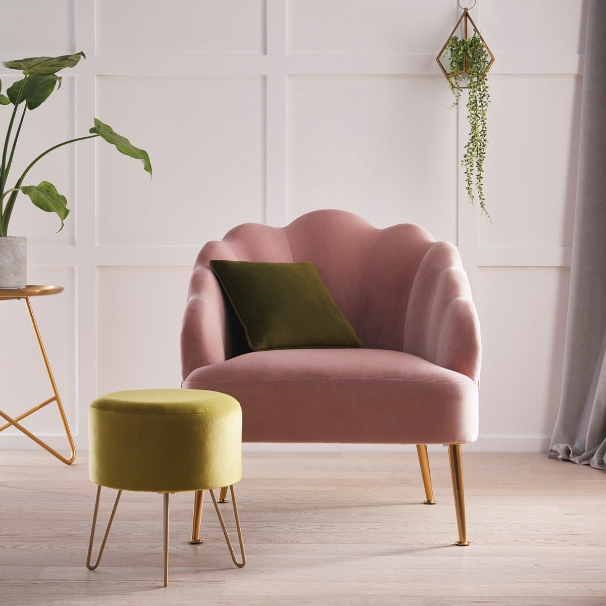 Pink armchair with a green cushion in a room with a plant and small table.