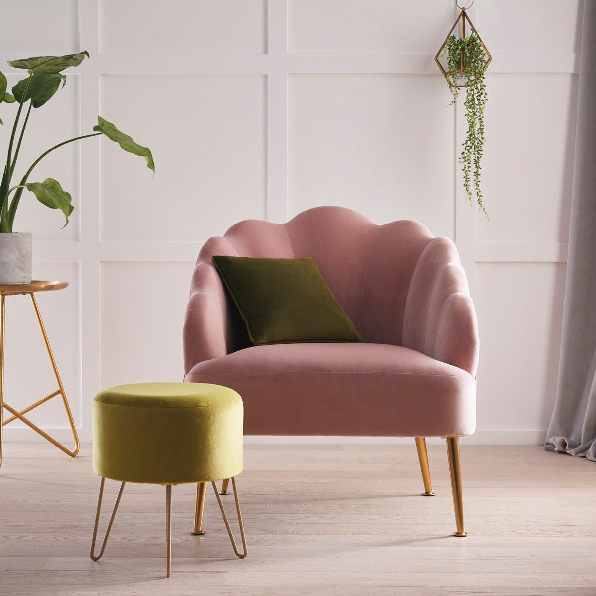 Pink armchair with a green cushion in a room with a plant and small table.