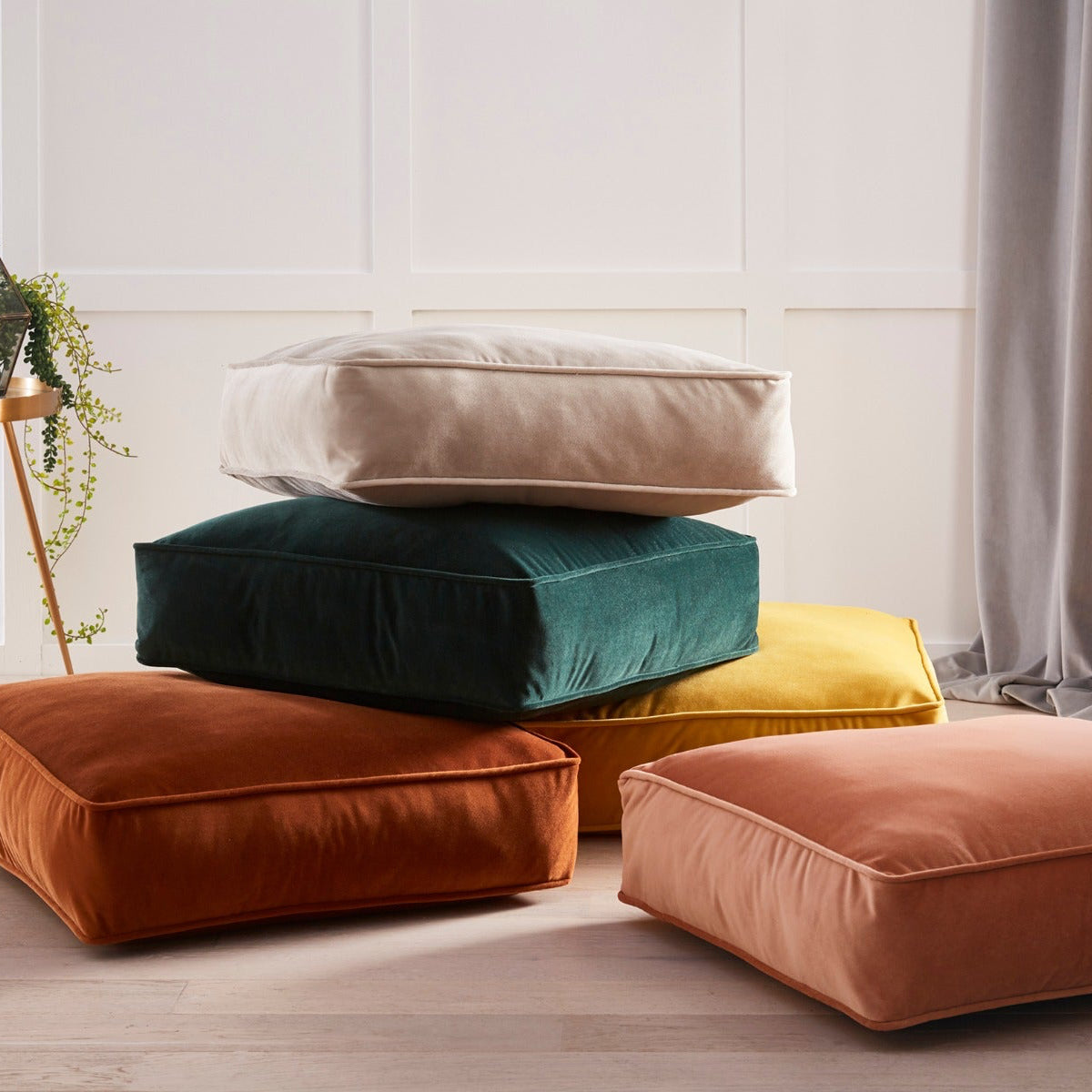 Stack of colorful cushions on a light wooden floor with a neutral wall background