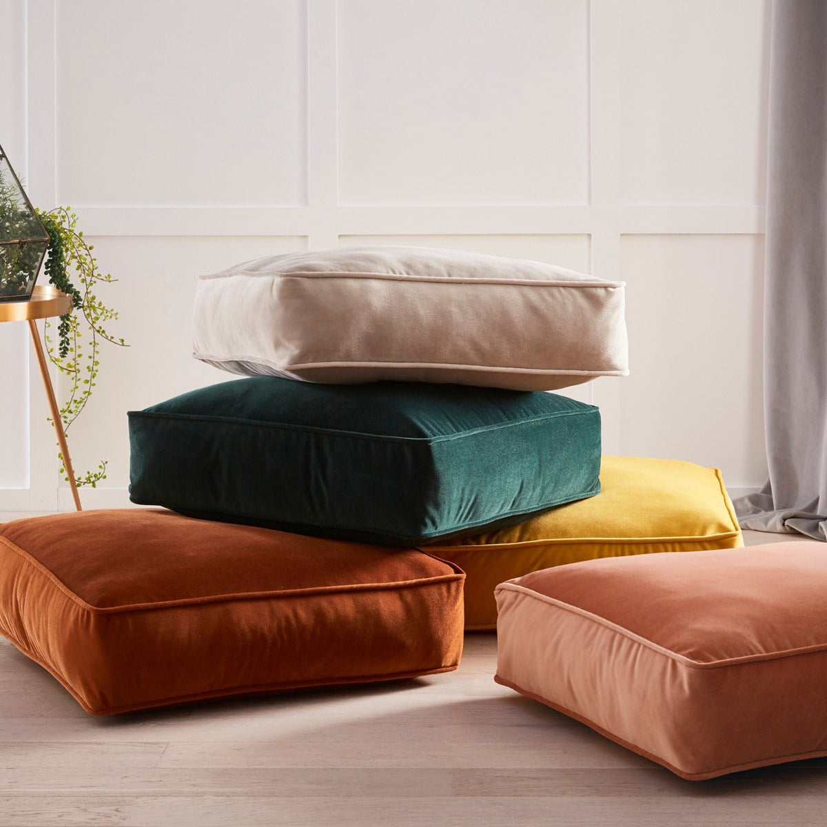 Stack of colorful cushions on a light wooden floor with a neutral wall background