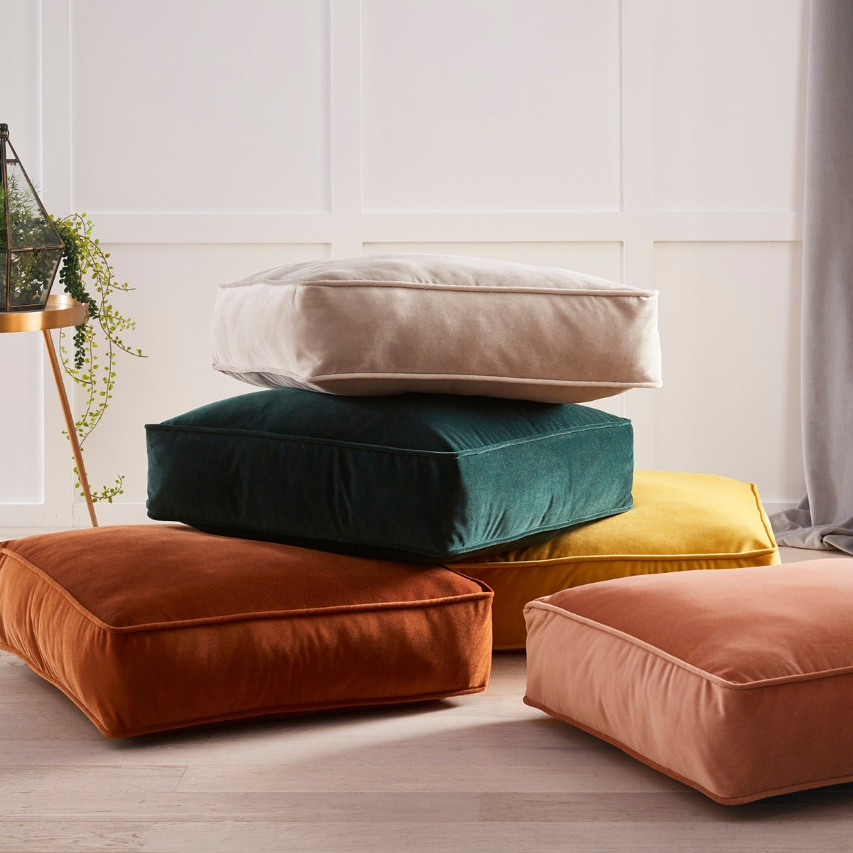 Stack of colorful cushions on a light wooden floor with a neutral wall background