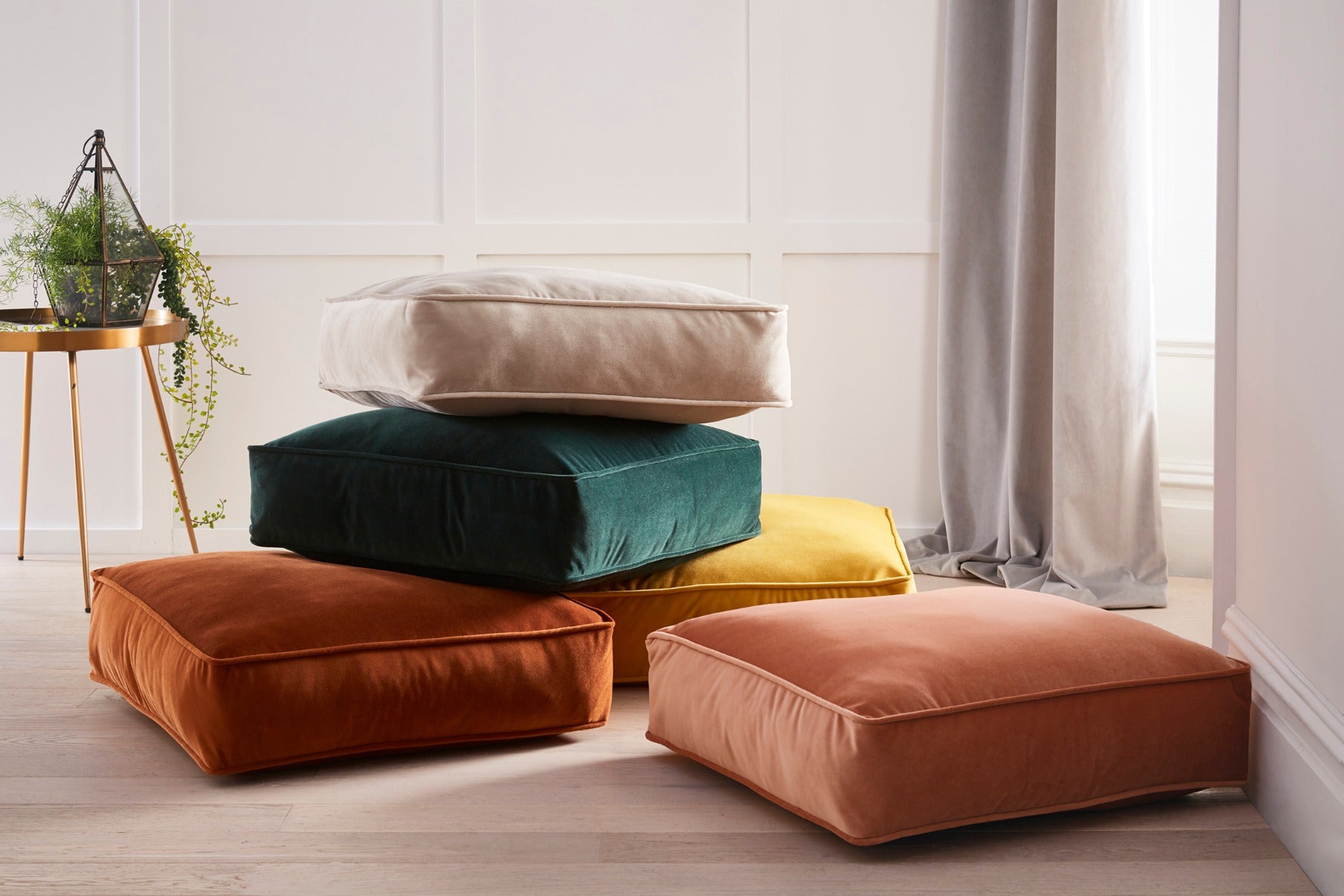 Stack of colorful cushions on a light wooden floor with a neutral wall background