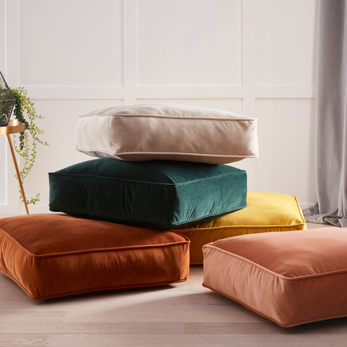 Stack of colorful cushions on a light wooden floor with a neutral wall background