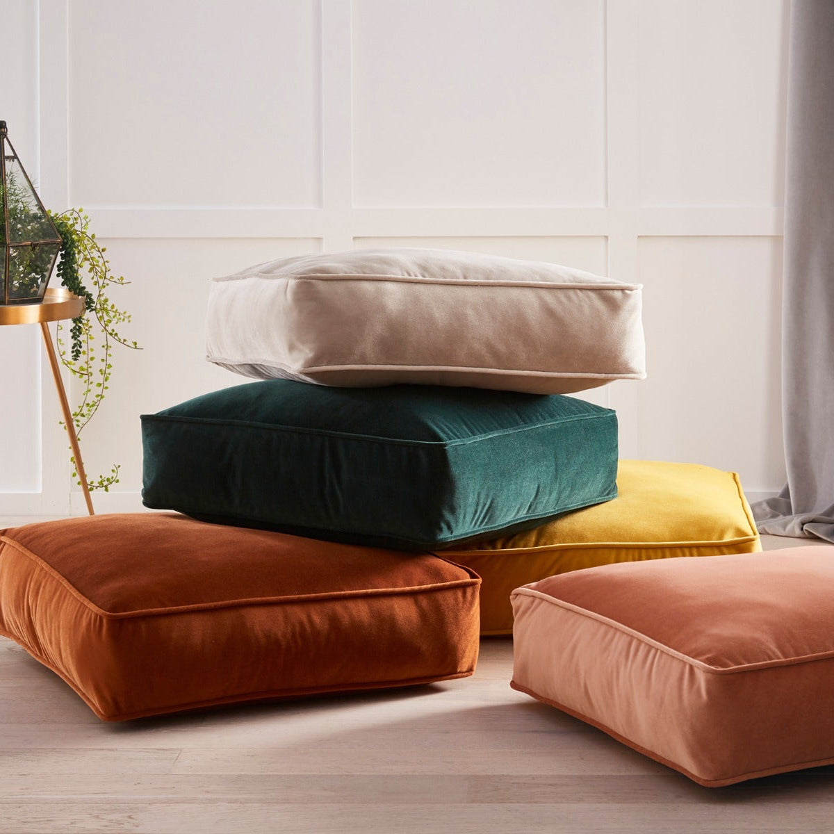 Stack of colorful cushions on a light wooden floor with a neutral wall background