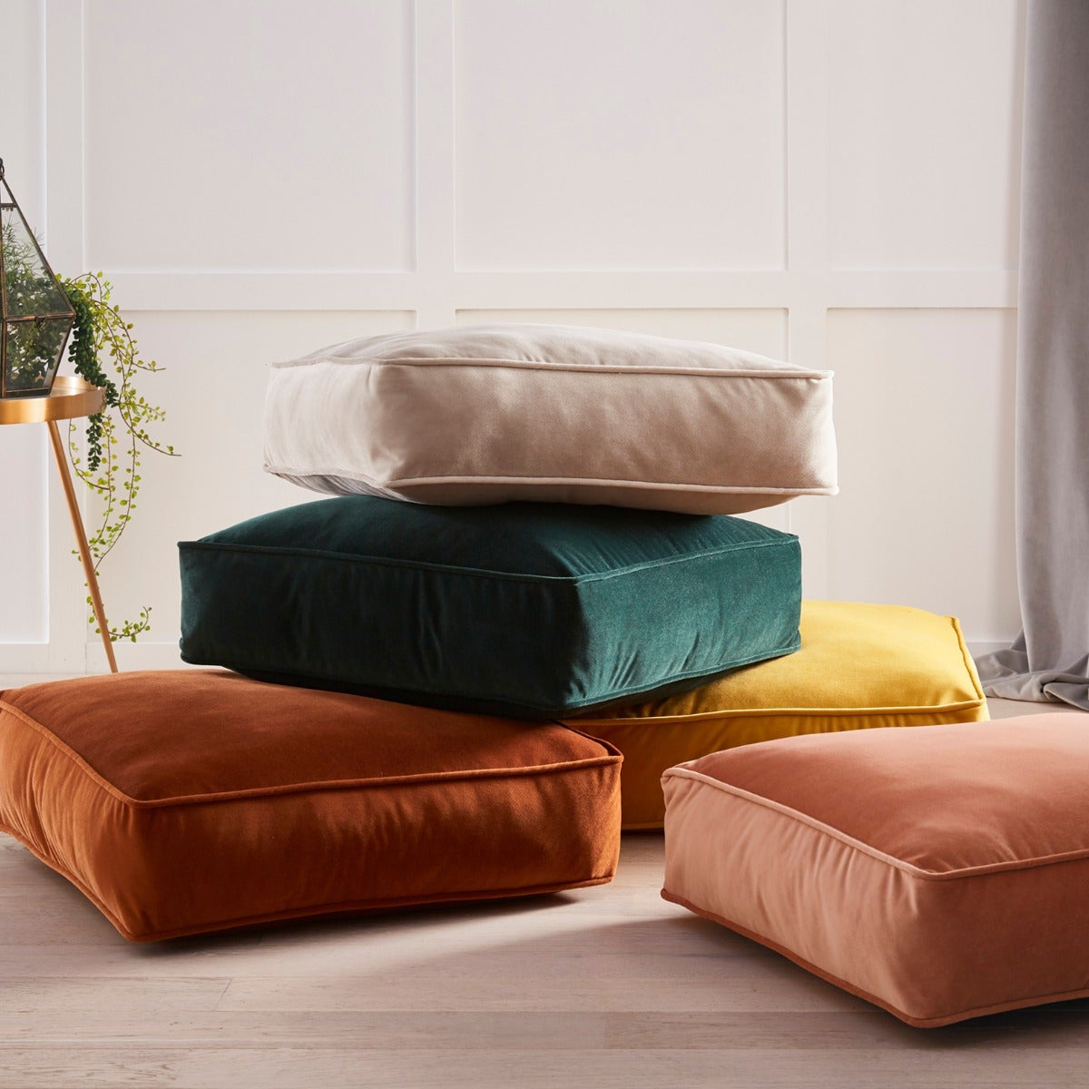 Stack of colorful cushions on a light wooden floor with a neutral wall background
