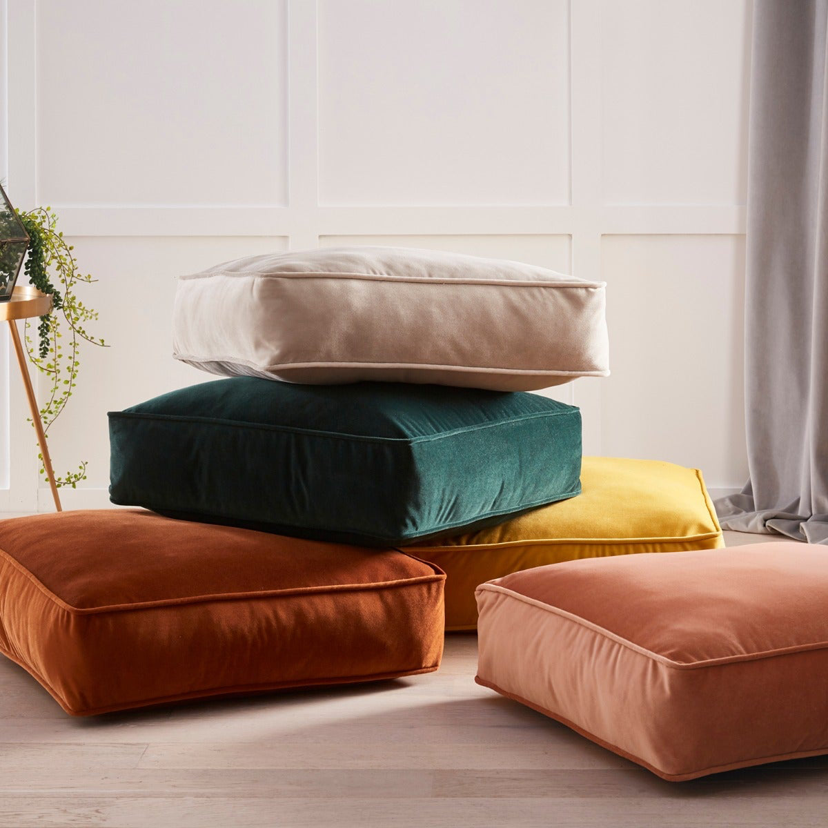 Stack of colorful cushions on a light wooden floor with a neutral wall background