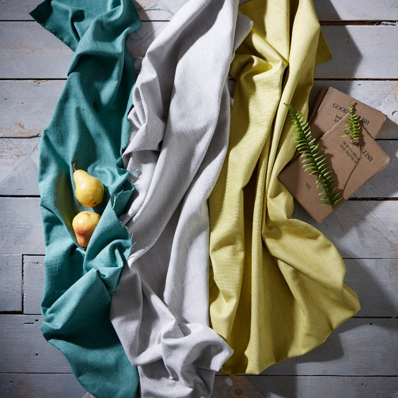 Three folded cloths in teal, white, and yellow on a wooden surface with a small plant.