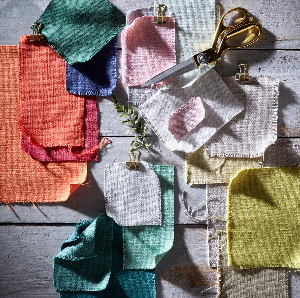 Color swatches with fabric samples in various colors and a pair of scissors on a wooden surface.