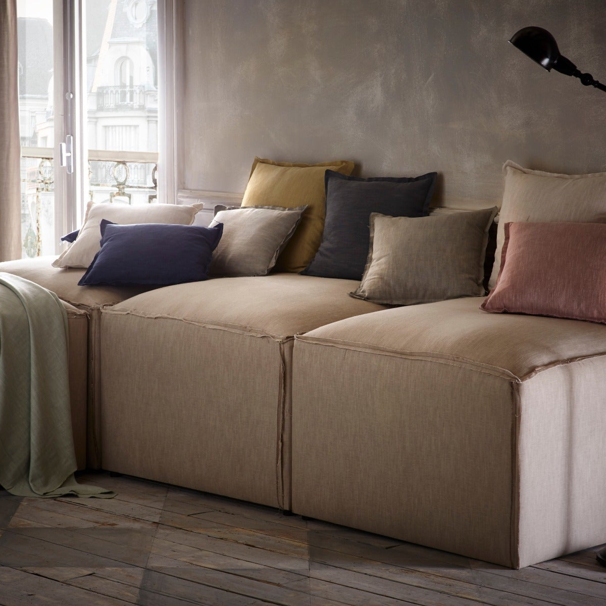 Beige sectional sofa with colorful pillows in a room with large windows.