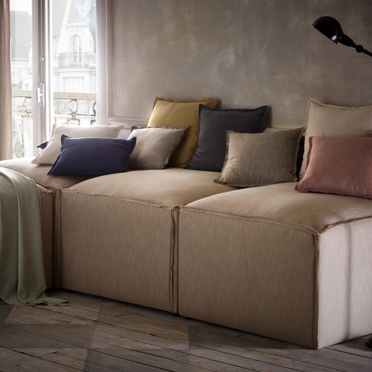 Beige sectional sofa with colorful pillows in a room with large windows.