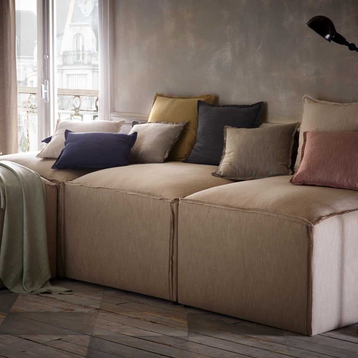 Beige sectional sofa with colorful pillows in a room with large windows.
