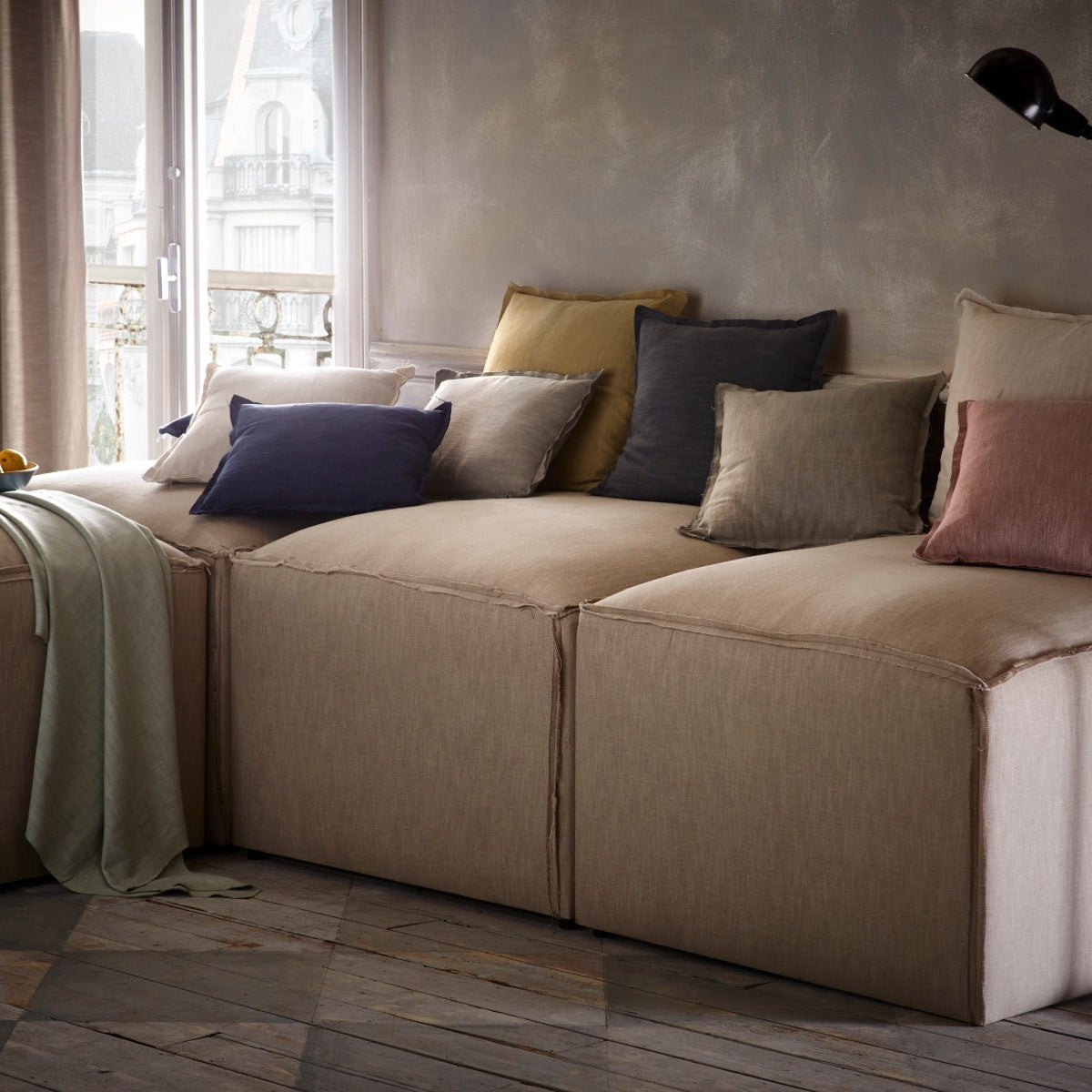 Beige sectional sofa with colorful pillows in a room with large windows.