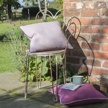 Decorative metal chair with cushions and a mug on a patio next to a brick wall.