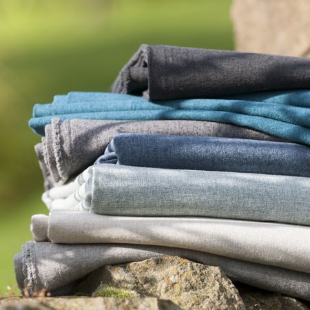 Stack of folded jeans in various colors on a stone surface with a blurred green background