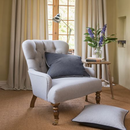 Gray armchair with a pillow in a room with curtains and a small table with a plant.
