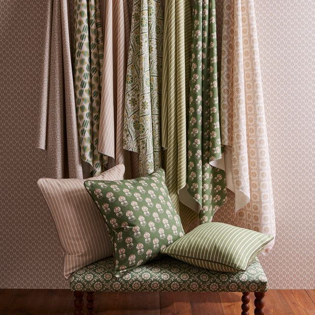 Fabric swatches hanging on a wall with a patterned bench and pillows below.