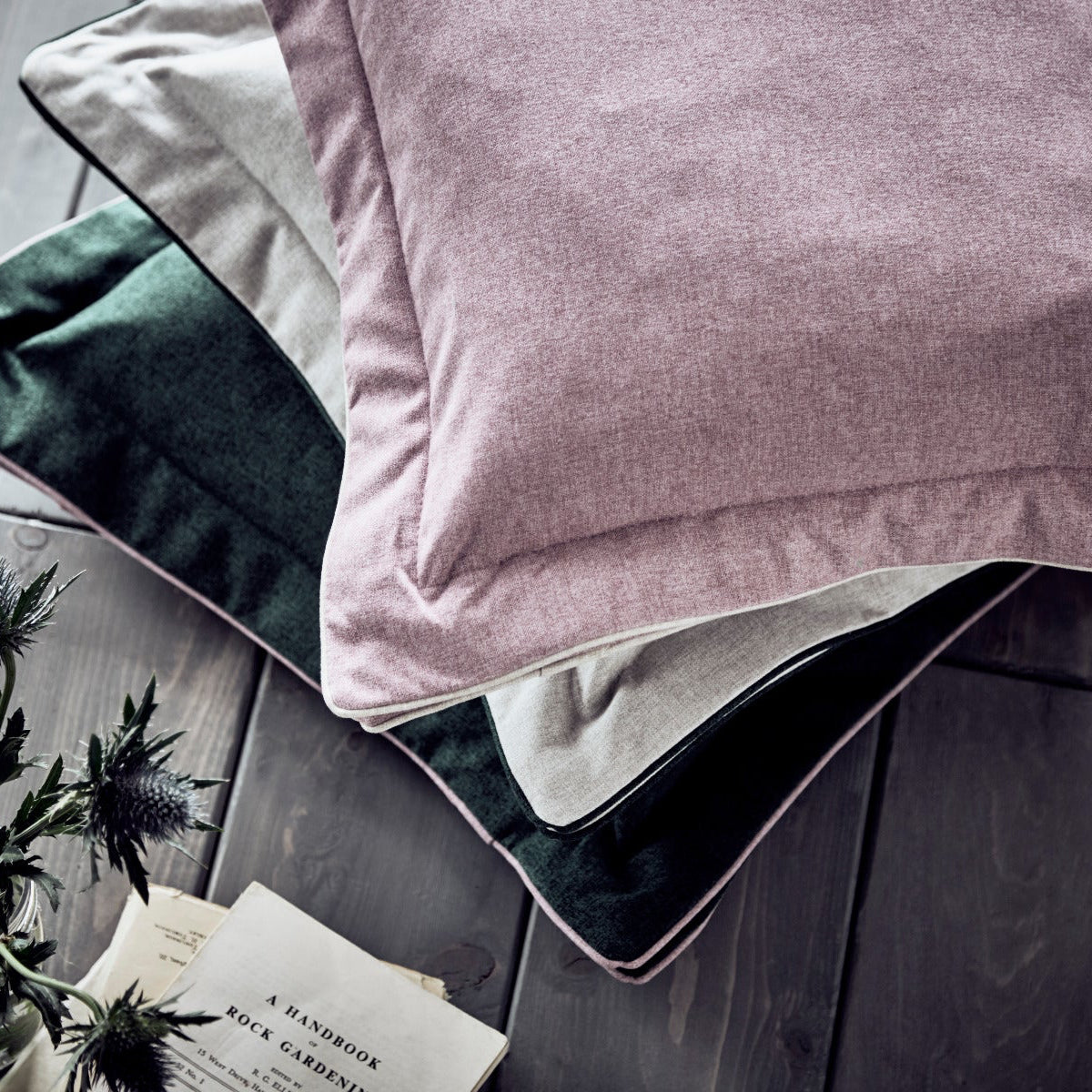 Pink pillow on a bed with a gray wooden floor and plant in the background
