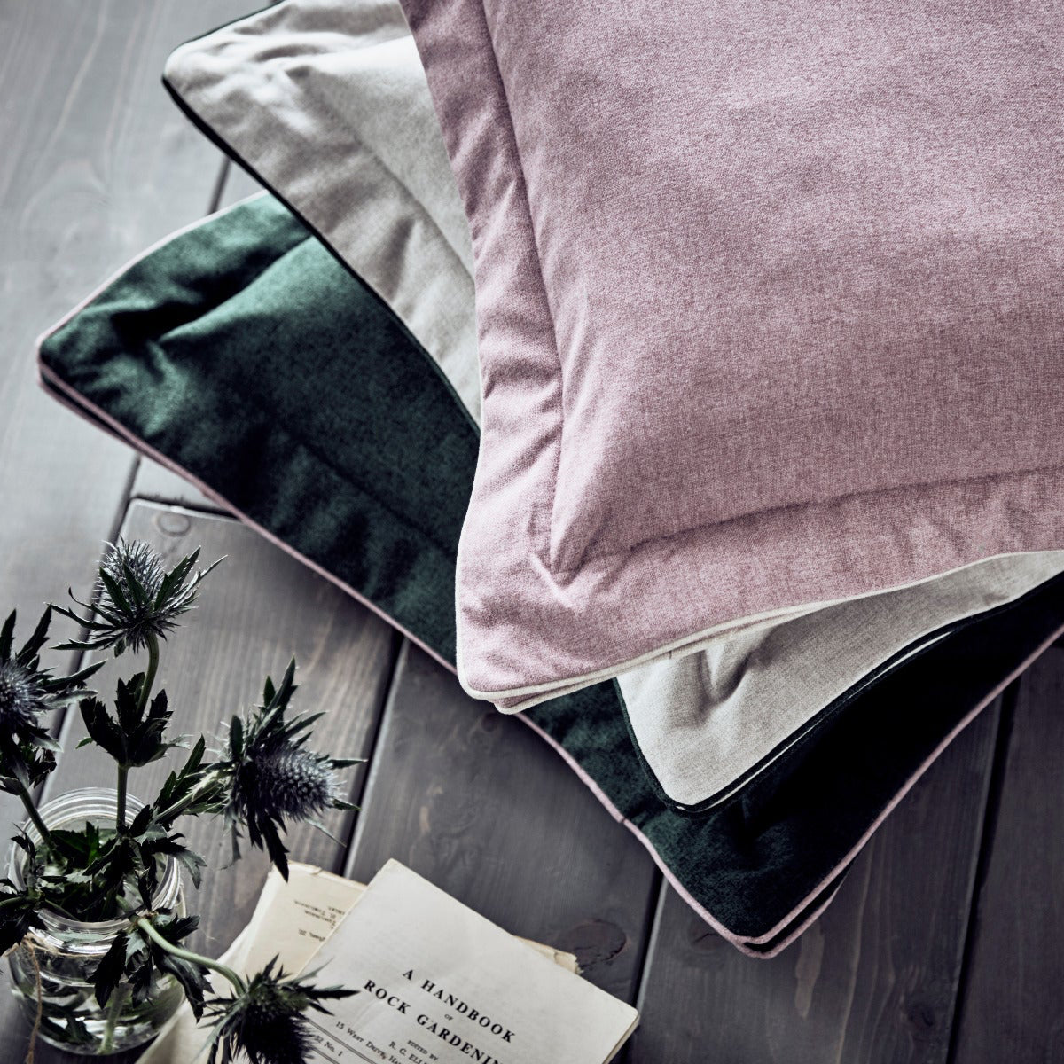 Pink pillow on a bed with a gray wooden floor and plant in the background