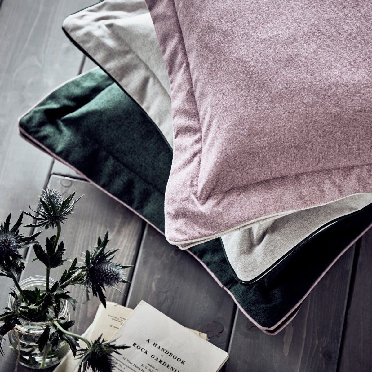 Pink pillow on a bed with a gray wooden floor and plant in the background