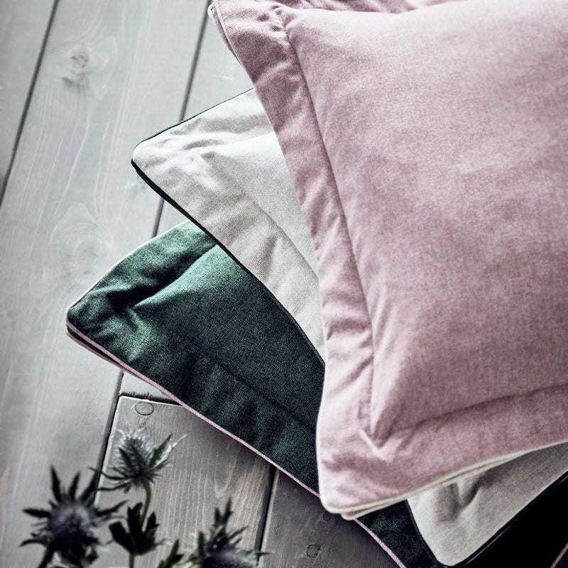 Stack of soft-textured pillows on a wooden surface with a small plant and book.