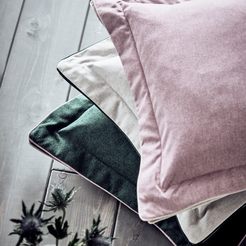 Stack of soft-textured pillows on a wooden surface with a small plant and book.