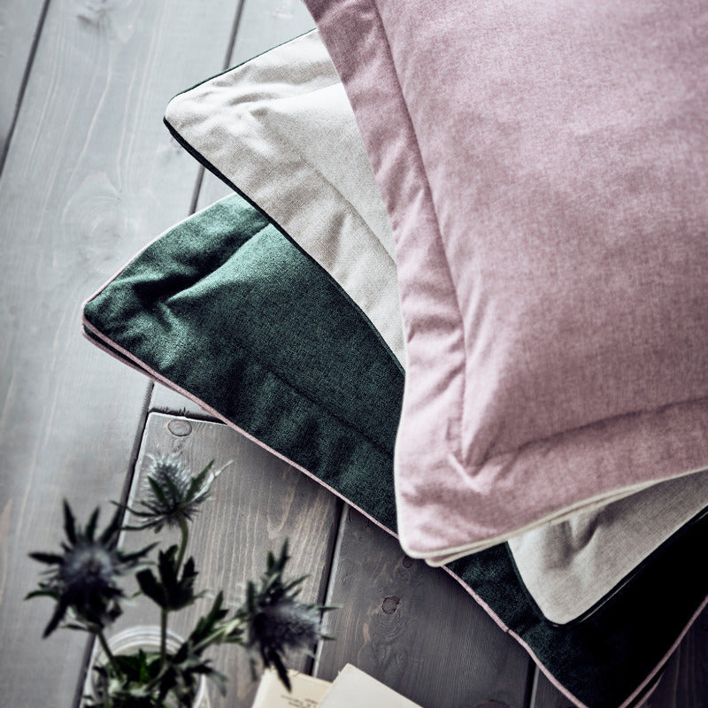 Stack of soft-textured pillows on a wooden surface with a small plant and book.